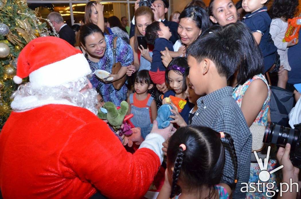 Santa Claus, flanked with excited kids for an early present.